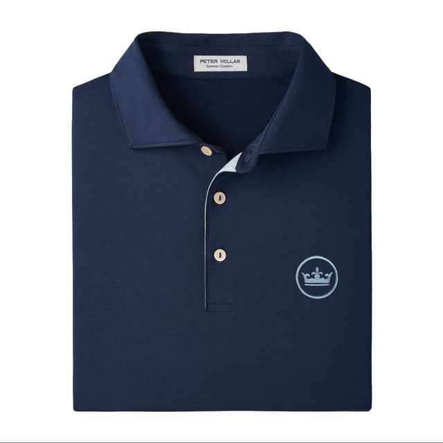 A folded navy blue polo shirt by Peter Millar, featuring a white embroidered crown logo on the left chest and a three-button placket.