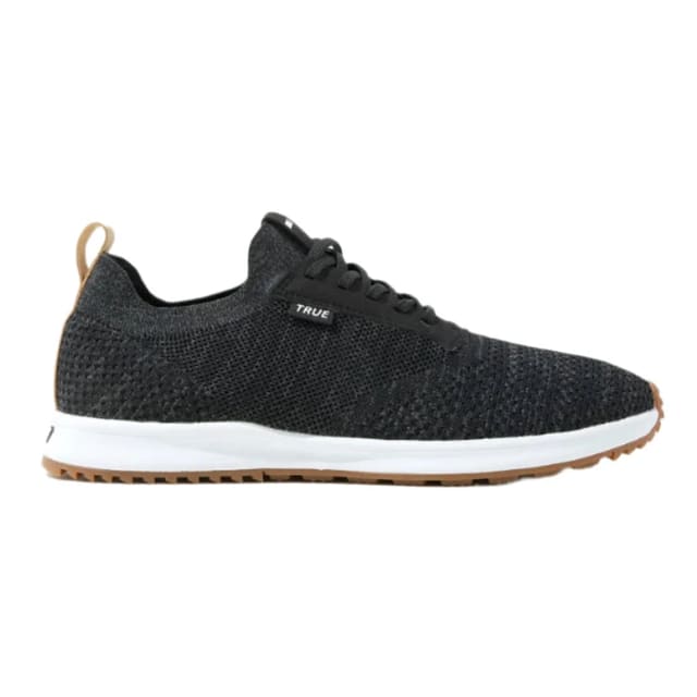 A pair of black TRUE Knit 2.0 unisex golf shoes with a breathable one-piece upper and a white sole.